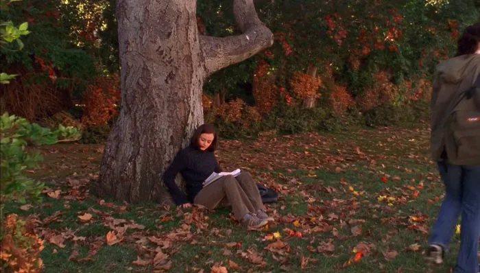 『ギルモア・ガールズ』で、キャンパスの紅葉した大きな木の前座って本を読むローリー
